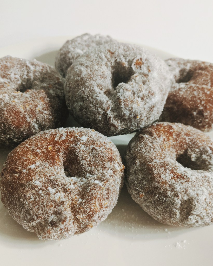 A stack of golden brown gluten-free donut rings coated with sugar on a white plate.
