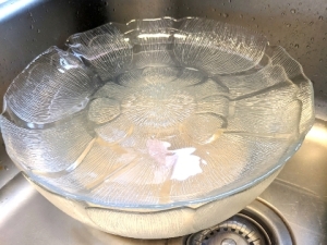 The glass bowl with the start of the gluten-free cardamom bun dough sat in a sink with warm water covered with a glass plate.