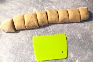 Pieces of gluten-free cardamom bun dough and a lime green dough scraper on a grey worktop.
