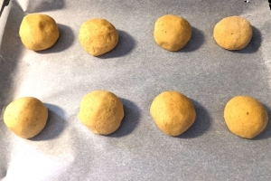 Balls of gluten-free cardamom bun dough on a baking tray with non-stick baking parchment about 20-30mm (roughly an inch) in between them.
