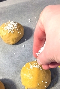 Kaukasian hand sprinkling white pearl sugar on the gluten-free cardamom buns brushed with egg prior to baking.
