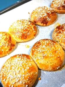 Golden brown large gluten-free buns with smooth surface, no cracks and white pearl sugar on top. The buns touch eachother slightly.