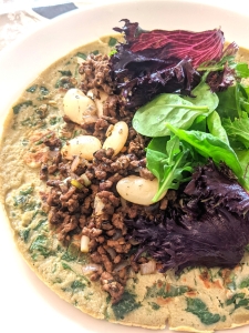 On the Right there is browned beef mince, butter beans, spring onion and colourful mixed leaves on top a gluten-free spinach pancake made with gluten-free Lovegrass Ethiopia ivory teff flour.