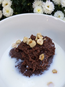 Dark brown gluten-free chocolate whipped porridge topped with toasted hazelnuts served with milk in a white bowl.