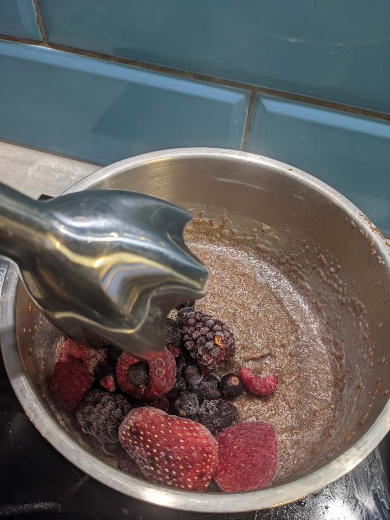 Adding frozen berries into the cooked teff porridge, a stick blender going in to blitz the berries and to whip the porridge fluffy and airy. 