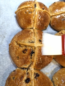 Golden brown hot cross buns being brushed with sugar syrup to give them a delightful sheen.