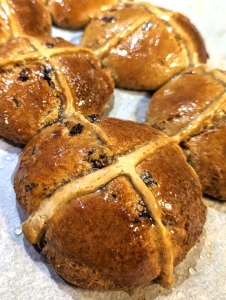 Close up of golden brown and glistening hot cross bun with raisins and currants showing through.