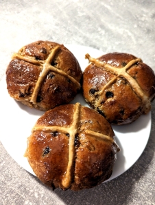 Three golden brown gluten-free hot cross buns topped with translucent sugar glaze on a white plate.