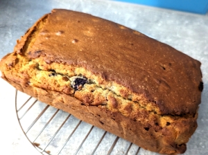 Golden brown gluten-free teff cake on a wire rack with blueberry peaking out of the crack across the top.